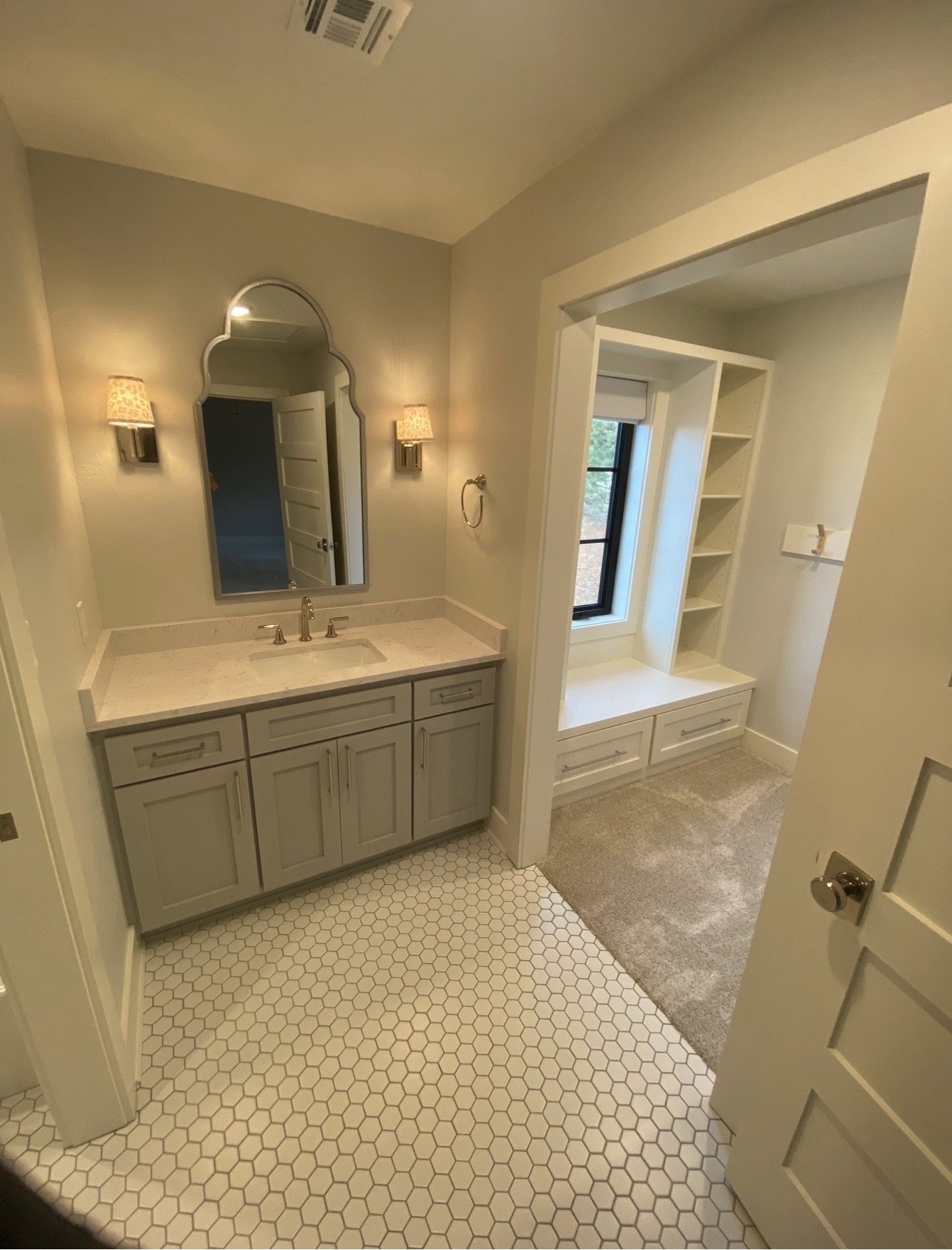 Painted bathroom vanity with stone countertop, wall sconces, and hexagonal tile flooring