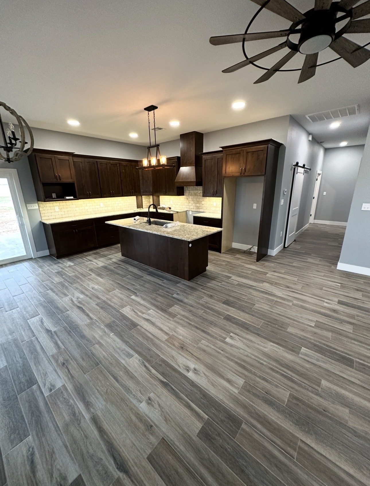 Finished kitchen with dark wood cabinetry, a large island, pendant lighting, and wood-look floors